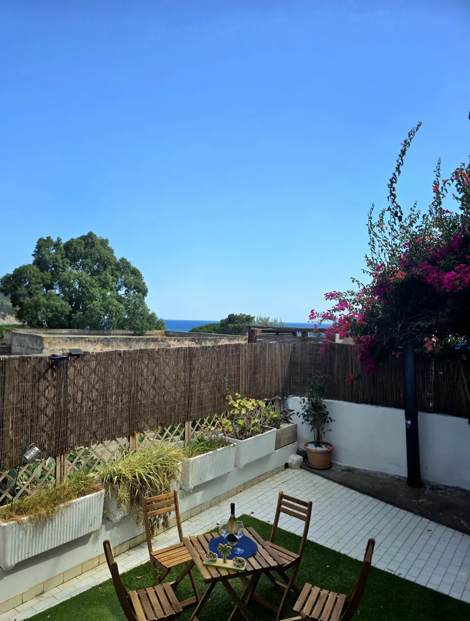 Die Gartenterrasse mit Tisch, Bougainvillea und einem Blick aufs Meer
